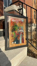 Framed abstract painting leaning against a brick wall.